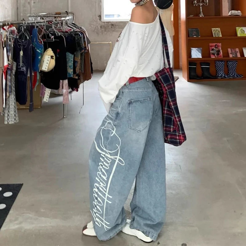 Woman wearing blue Y2k baggy boyfriend jeans with a white graphic print on the side leg.