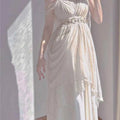 Ankle-length white knit dress with spaghetti straps, draped layers, and a gold ring belt.