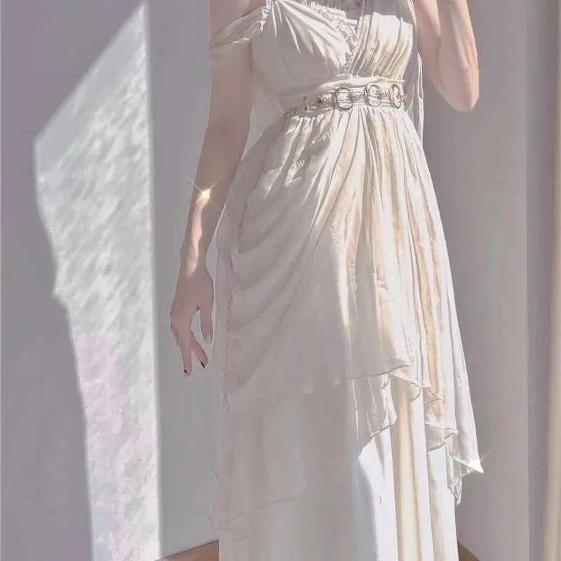 Ankle-length white knit dress with spaghetti straps, draped layers, and a gold ring belt.