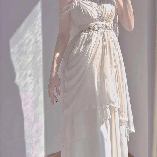Ankle-length white knit dress with spaghetti straps, draped layers, and a gold ring belt.